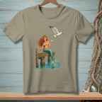 Mermaid with red hair sitting on a dock with a seagull flying overhead.