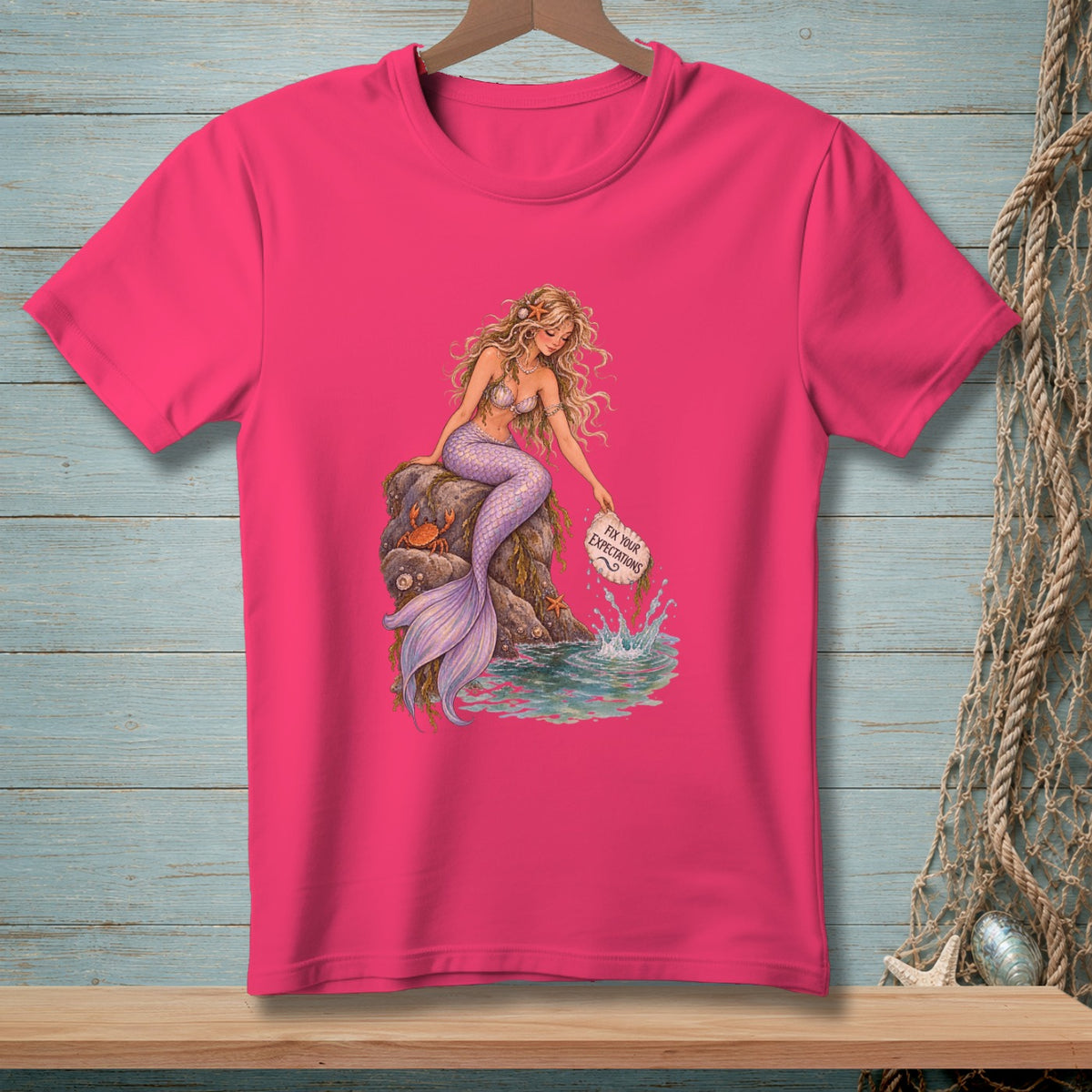 Pink t-shirt featuring a mermaid sitting on a rock with "Fix Your Expectations" text.