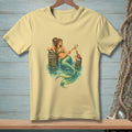 Light yellow t-shirt with a detailed illustration of a mermaid and a crab by the water.