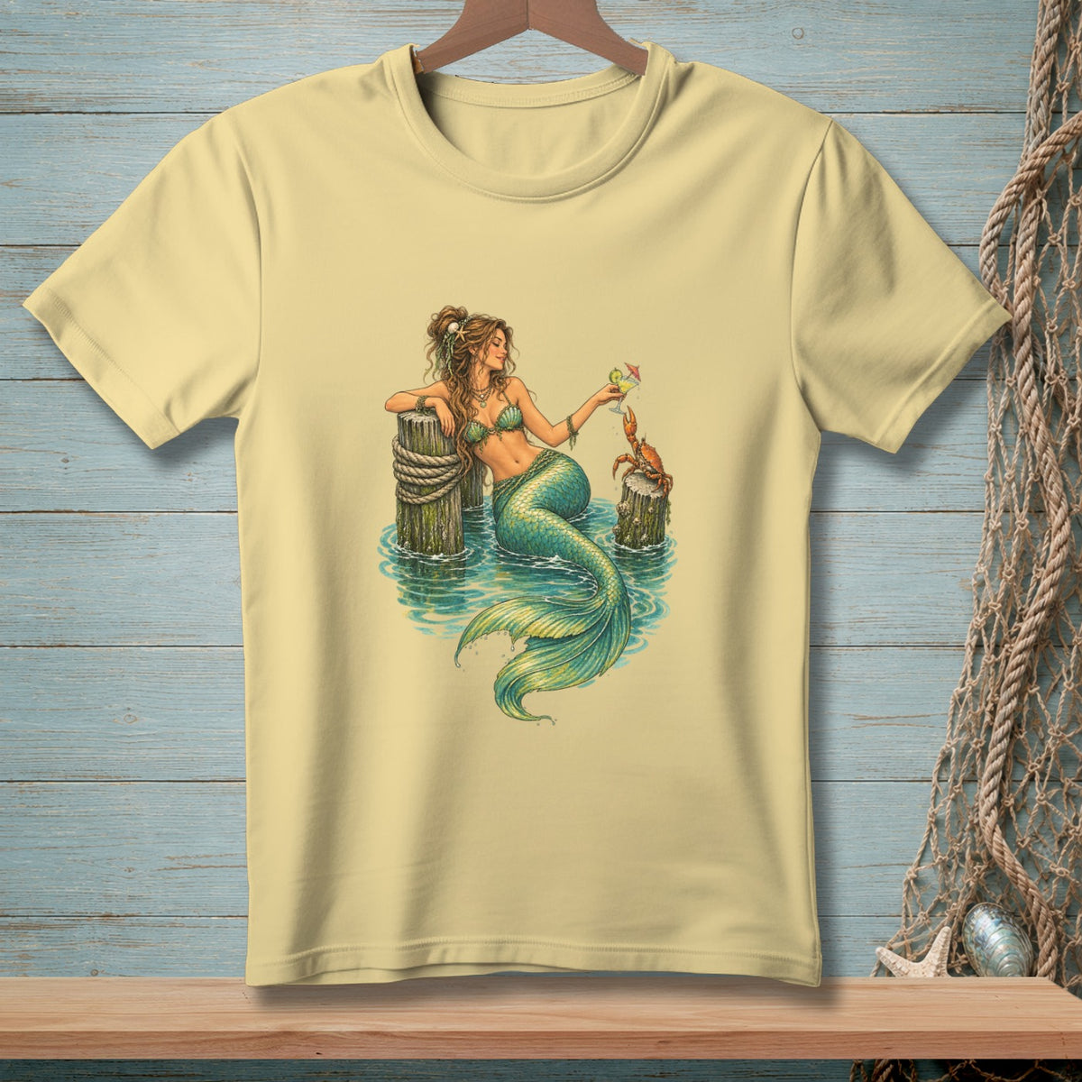 Light yellow t-shirt with a detailed illustration of a mermaid and a crab by the water.
