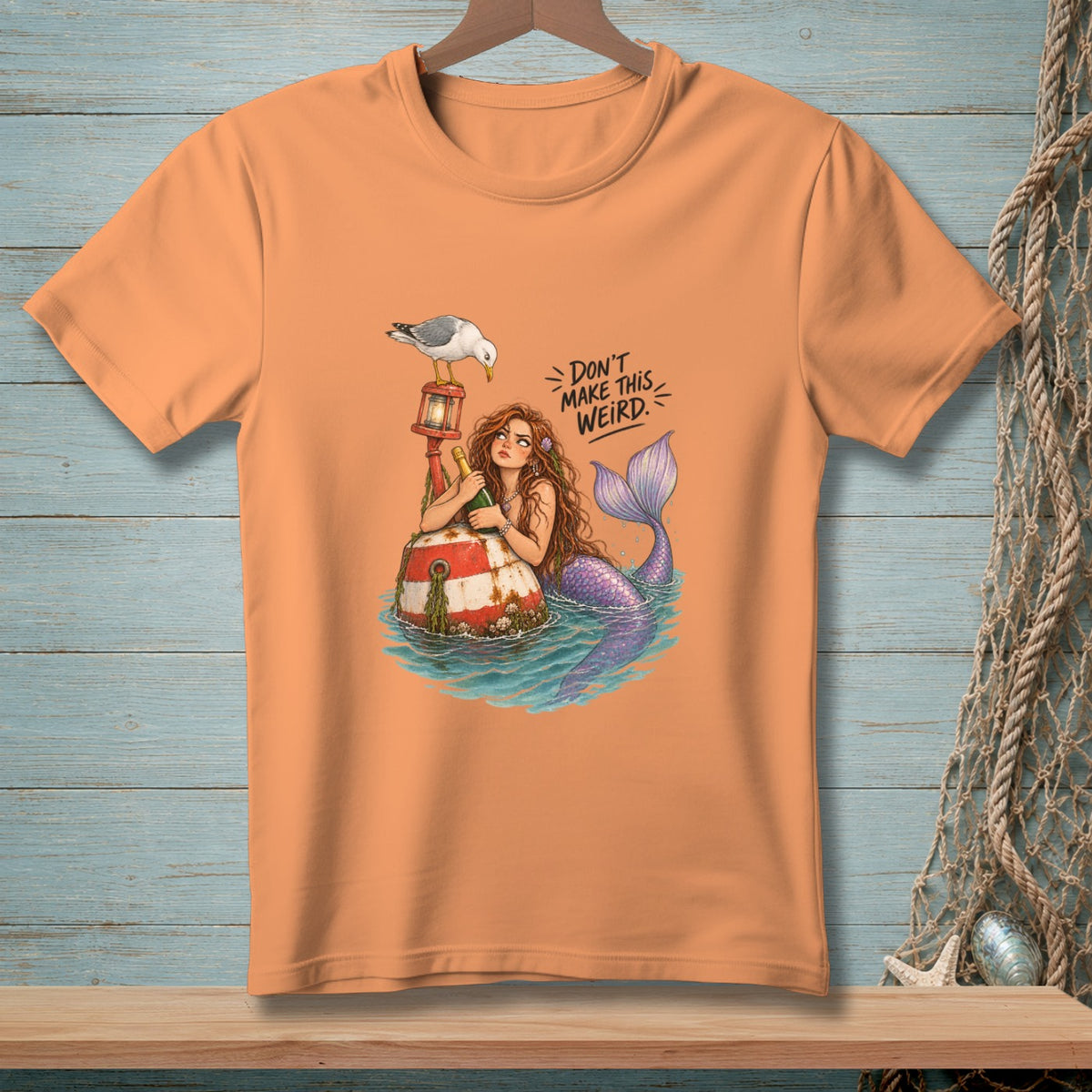Peach t-shirt with mermaid and seagull, reads "DON'T MAKE THIS WEIRD."