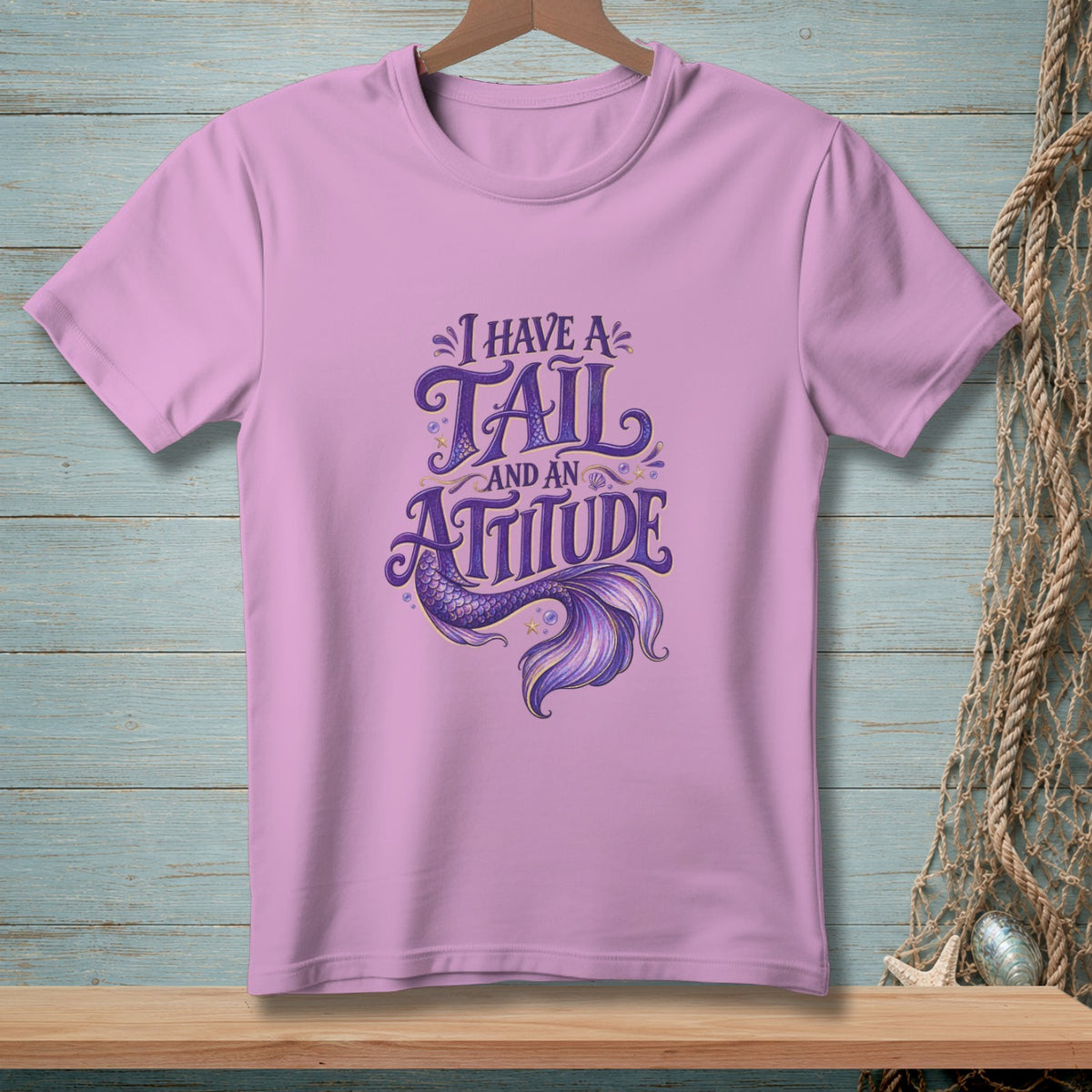 Lilac t-shirt with purple text and mermaid tail graphic reading "I have a tail and an attitude".