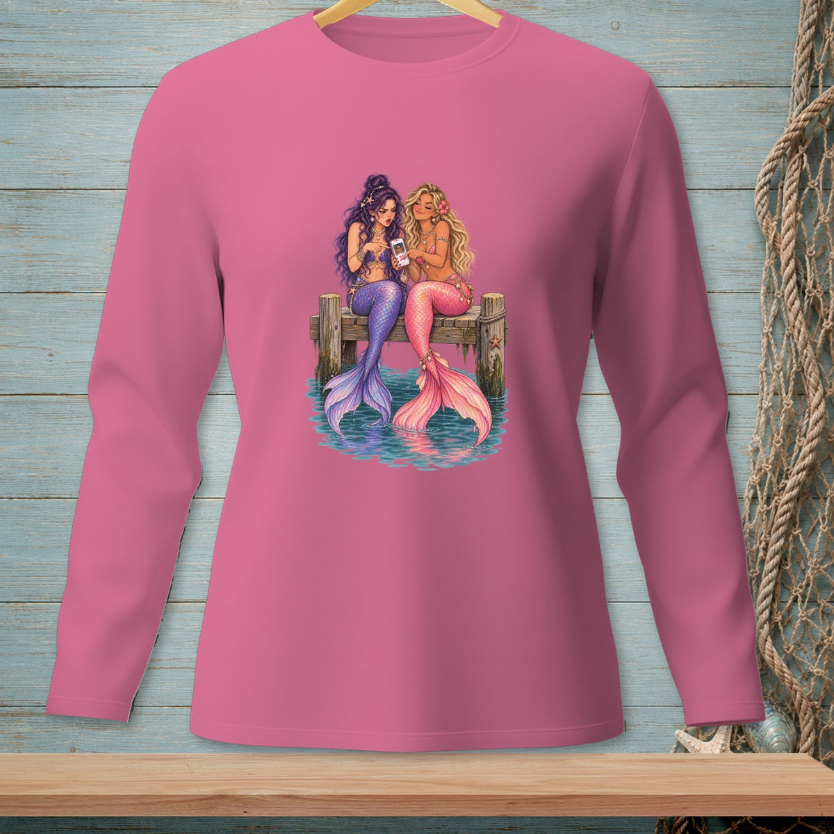Two mermaids sit on a dock using their phones.