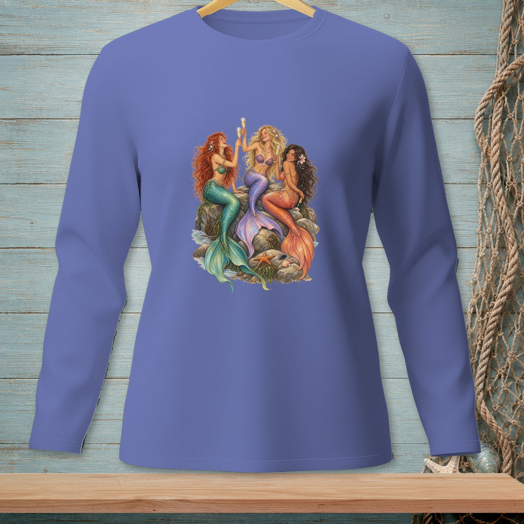 Three mermaids with colorful tails sit on rocks, toasting with champagne flutes.