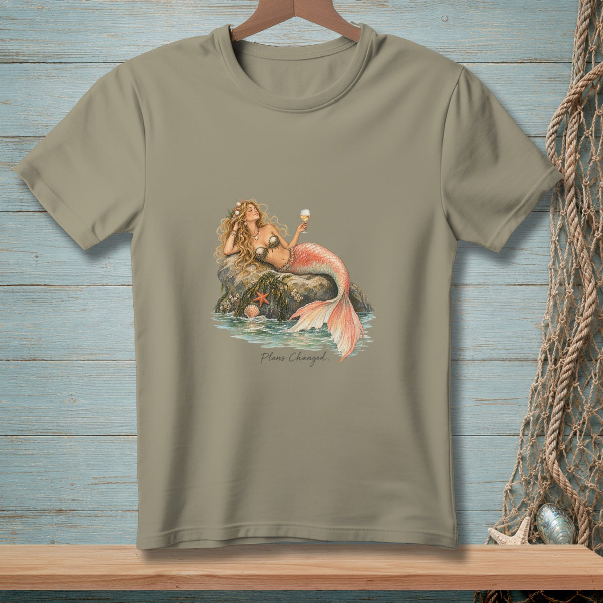 T-shirt with a mermaid holding a glass of champagne on a rock, text reads "Plans Changed."