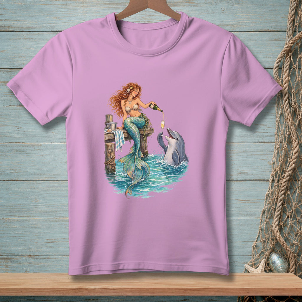 Mermaid pours champagne for a dolphin on a dock with ocean waves.