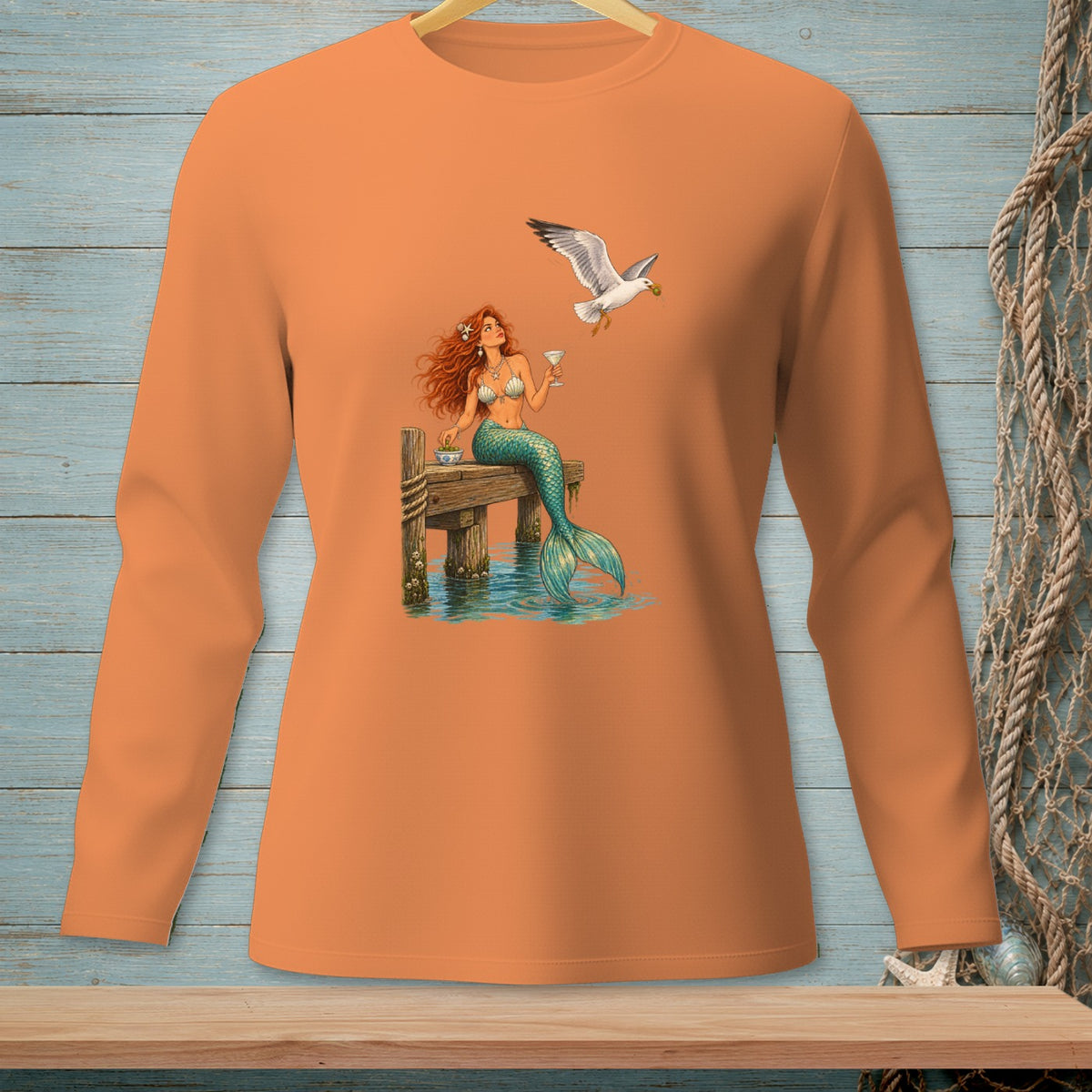 Long-sleeved shirt with a mermaid and seagull on a wooden dock with a drink.