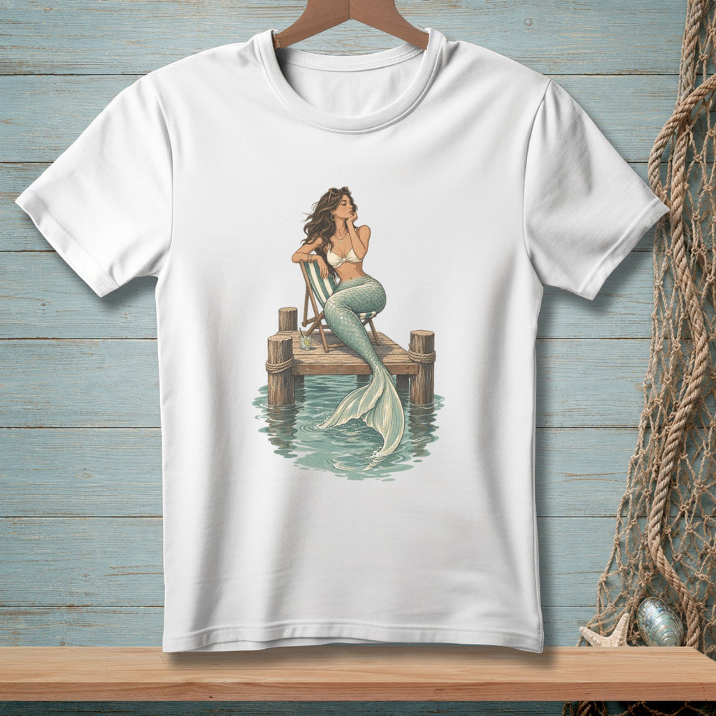 White t-shirt graphic of a mermaid sitting on a pier with a striped chair.