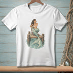 White t-shirt graphic of a mermaid sitting on a pier with a striped chair.