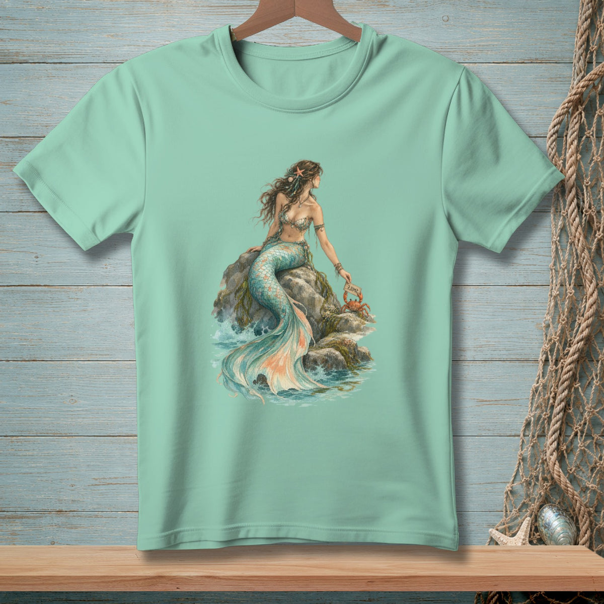Mint t-shirt with a mermaid sitting on a rock with a crab holding a "Smile" sign.