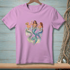 Three mermaids with tails in water, holding drinks on a pink t-shirt.