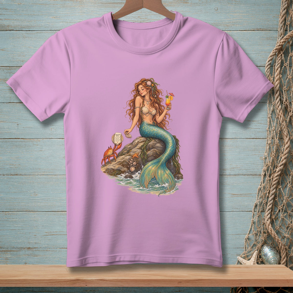 Pink t-shirt with a print of a mermaid holding a drink, sitting on a rock with a crab.