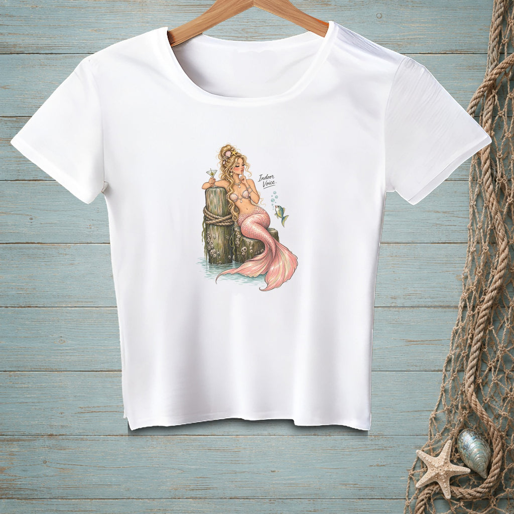 White t-shirt with a mermaid graphic holding a drink next to a wooden post.