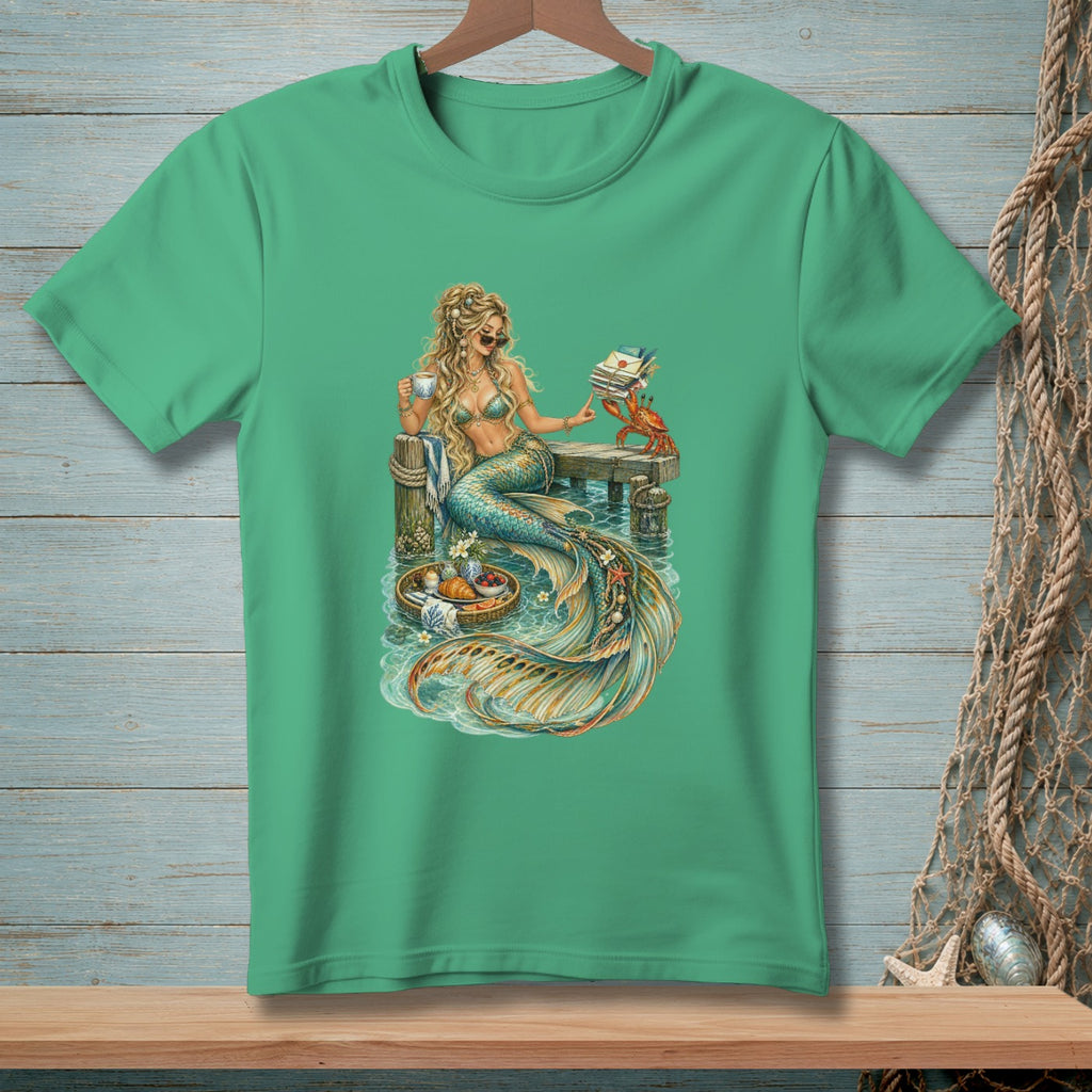 Mermaid with coffee and book on dock with crab, basket of pastries and fruit.