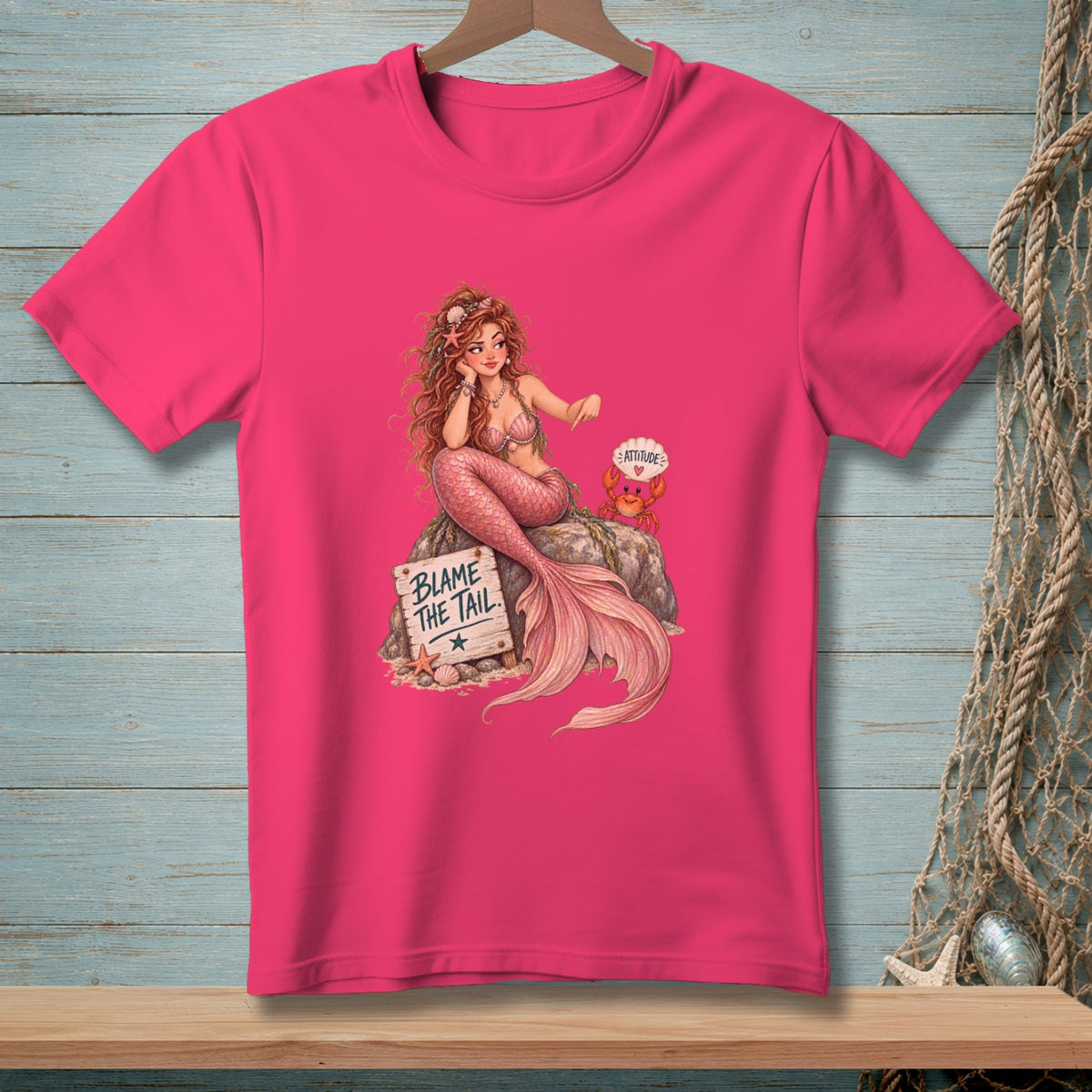 Mermaid with pink tail on rock with "BLAME THE TAIL" sign and crab.