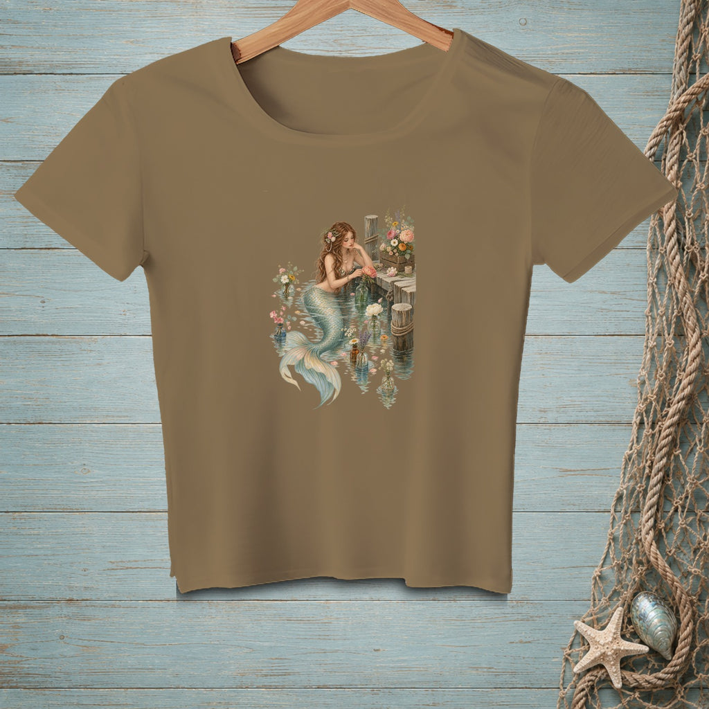 Brown t-shirt with a graphic of a mermaid among flowers on a wooden dock.