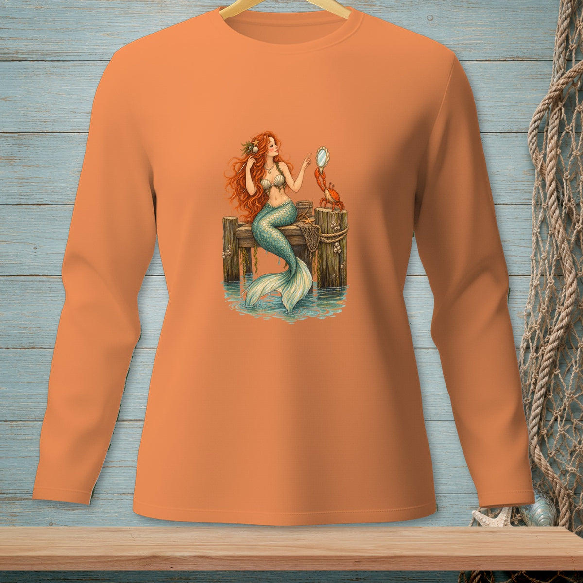 Orange long-sleeve shirt with a graphic of a mermaid and crab on a dock.
