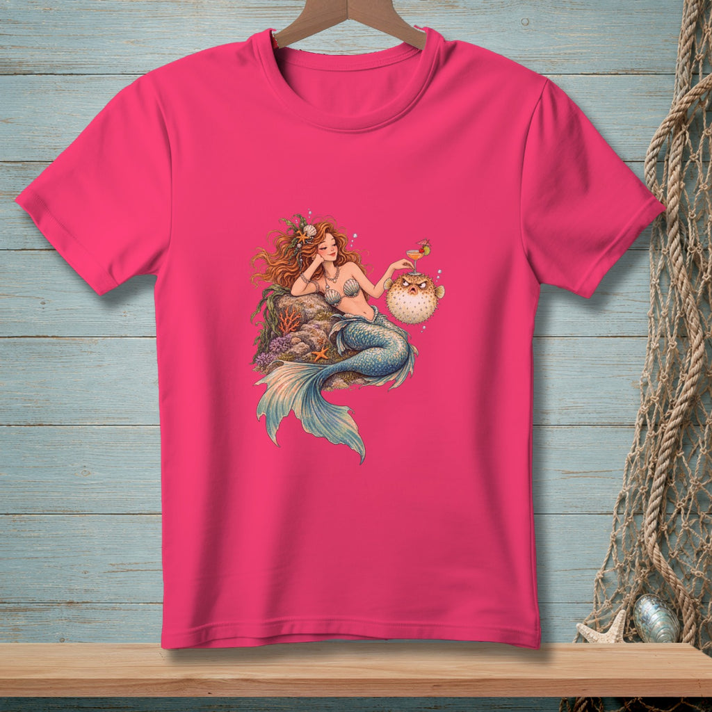 Pink t-shirt with mermaid lounging by a pufferfish holding a drink.