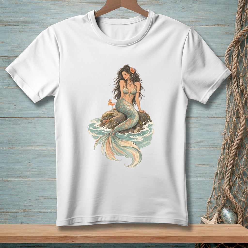 White t-shirt featuring a mermaid sitting on a rock in the ocean with a drink.