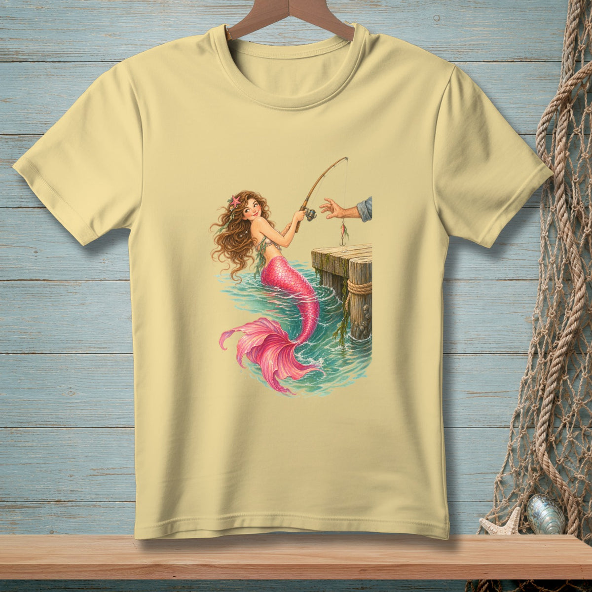 Light yellow t-shirt with illustration of a mermaid fishing from a dock.