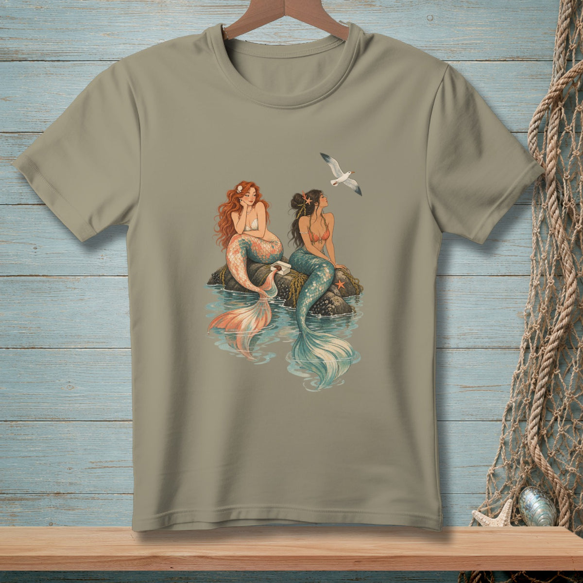 Two mermaids sit on rocks in the ocean with a seagull flying overhead.