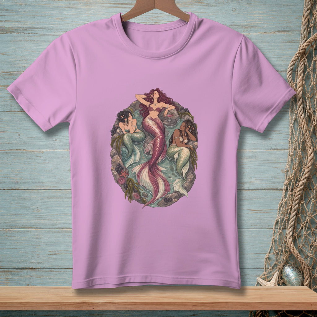 Three mermaids resting in a circular sea-themed graphic on a pink t-shirt.