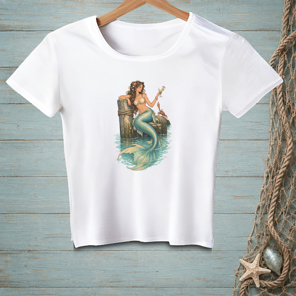 White t-shirt with a mermaid holding a drink, sitting on a pier post with a crab.
