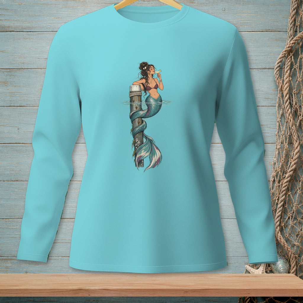 Long sleeve blue t-shirt with a mermaid sitting on a wooden post drinking a beverage.