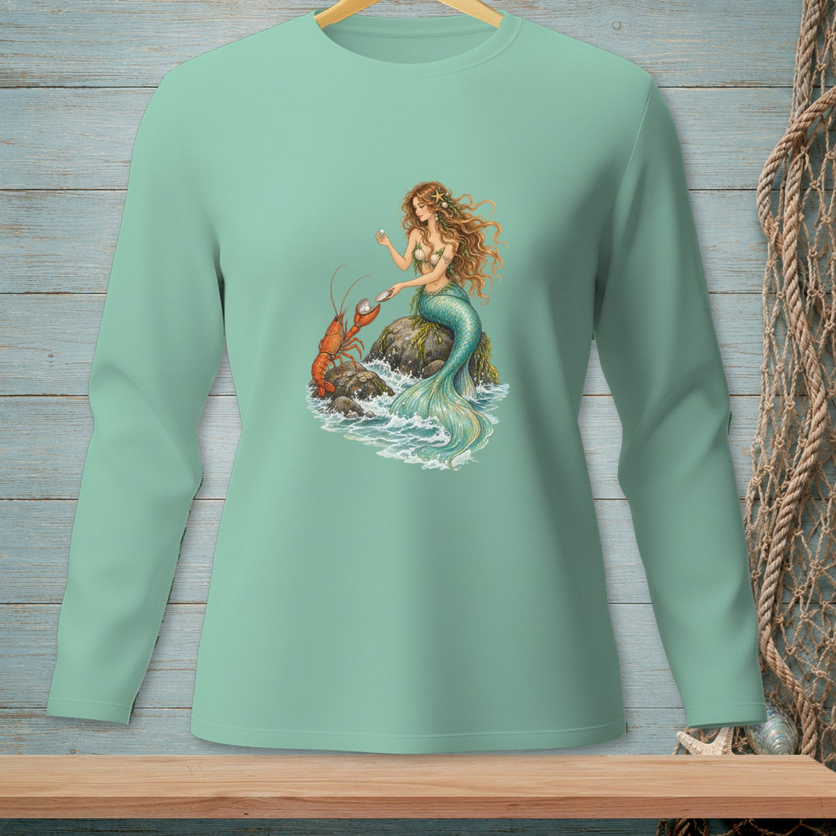 Mint green long-sleeve shirt with mermaid and lobster graphic on a rock.