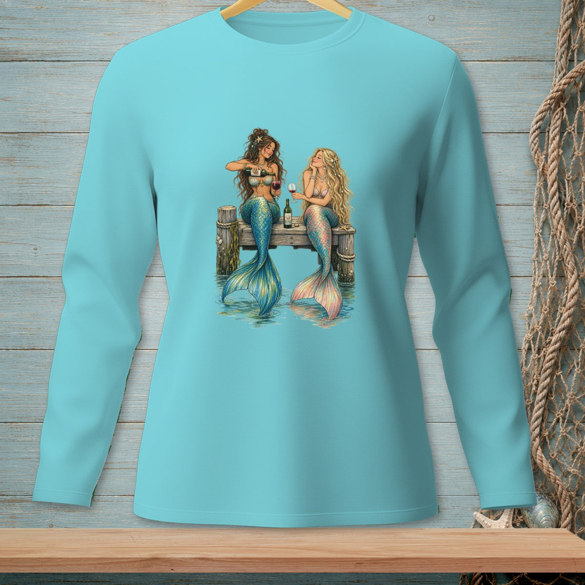 Two mermaids sit on a dock, drinking wine by the water.
