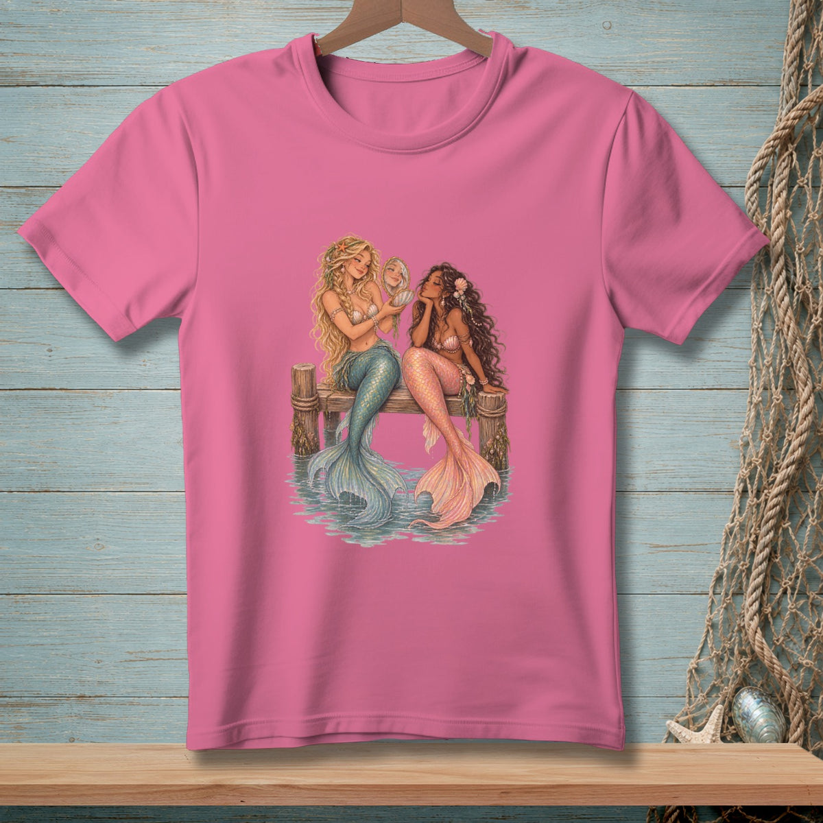 Two mermaids with colorful tails sit on a wooden dock, one looking in a mirror.
