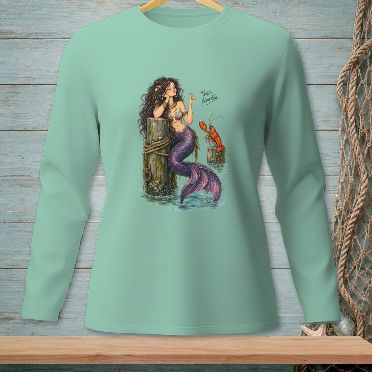 Mermaid holding pearl by pier, lobster nearby, text "That's Adorable".