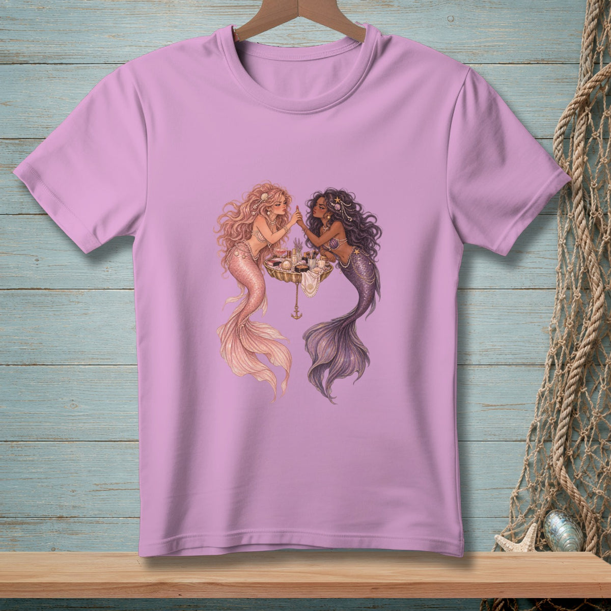 Two mermaids are applying makeup from a vanity on a lavender t-shirt.