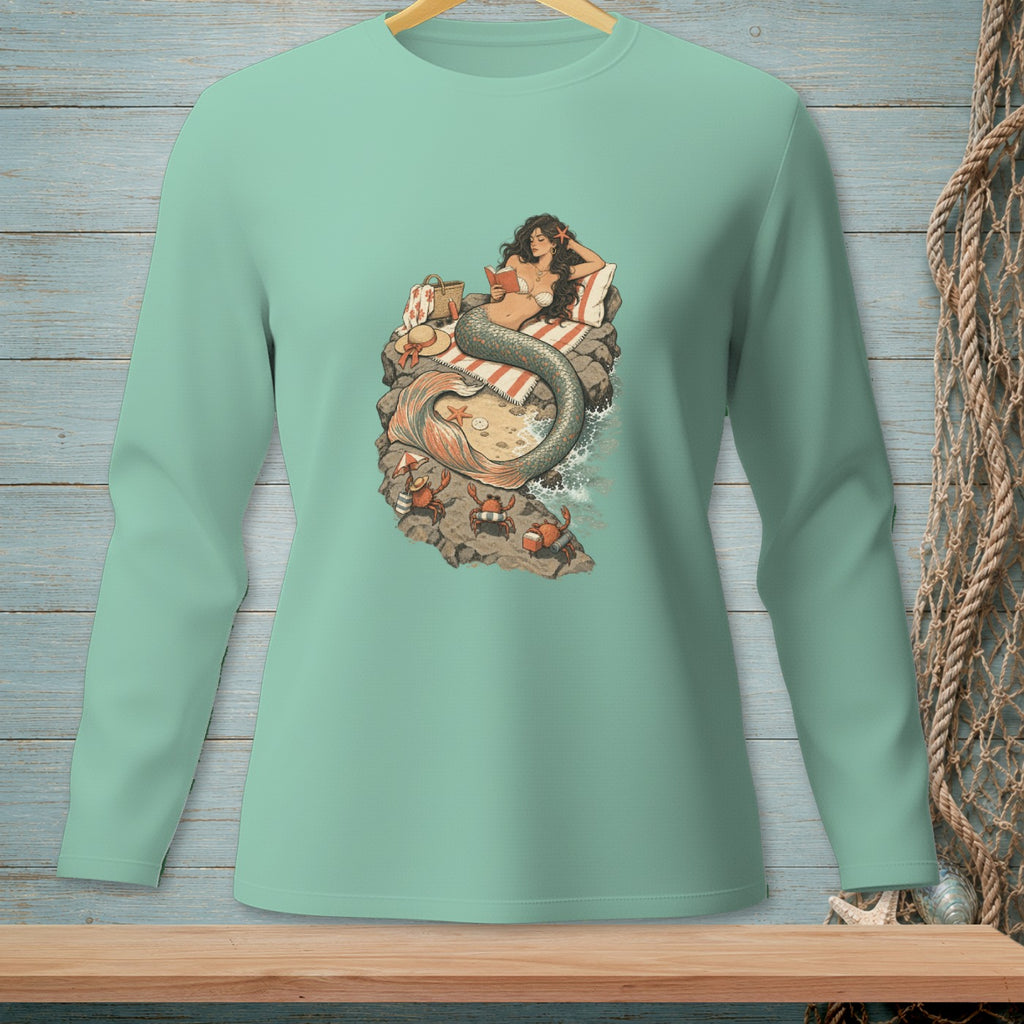 Mermaid reading on a rock with crabs on a beach, displayed on a mint green long-sleeve shirt.