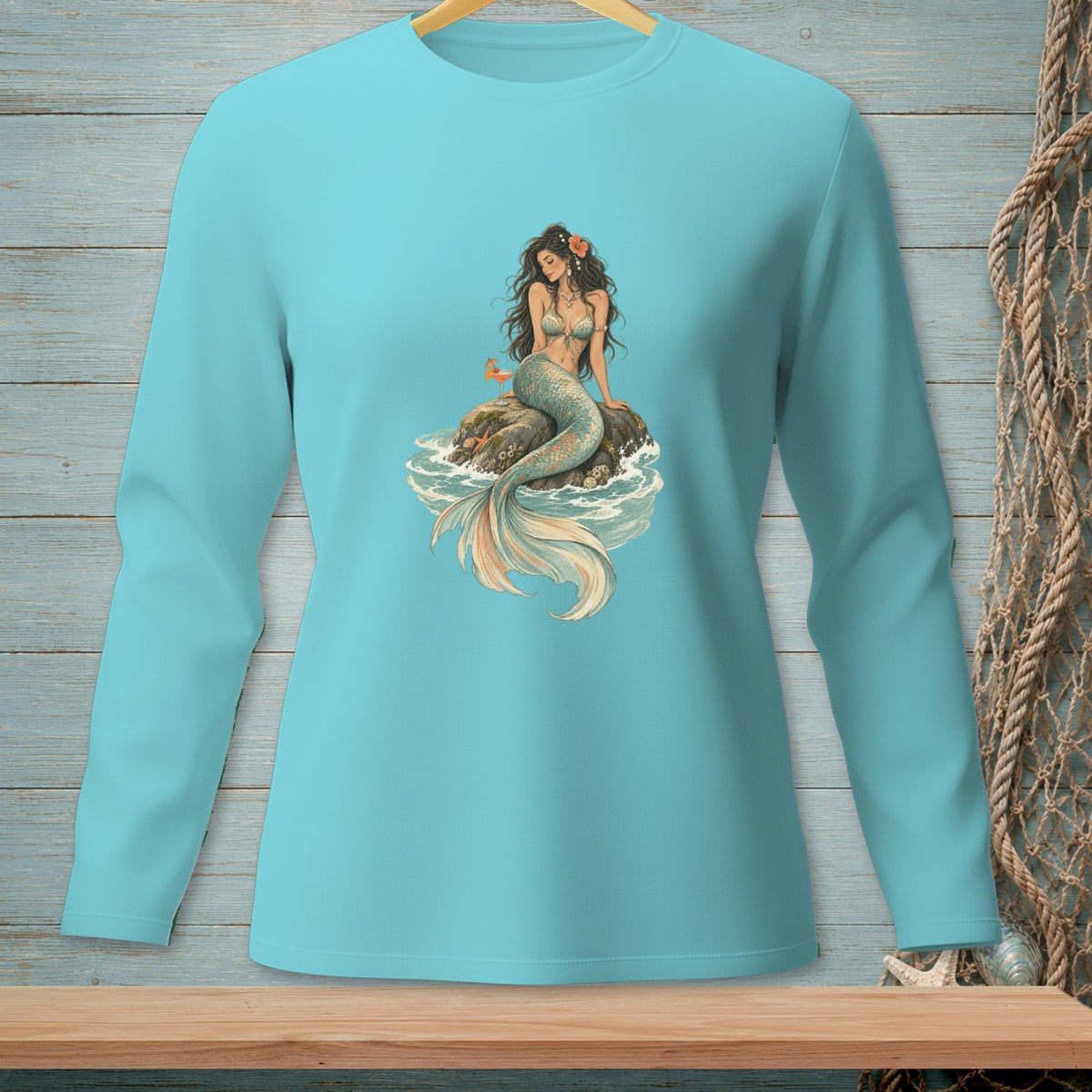 Long-sleeve teal shirt featuring a seated mermaid with a colorful tail and flower in her hair.