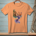 Peach t-shirt with a mermaid and octopus relaxing by a dock.