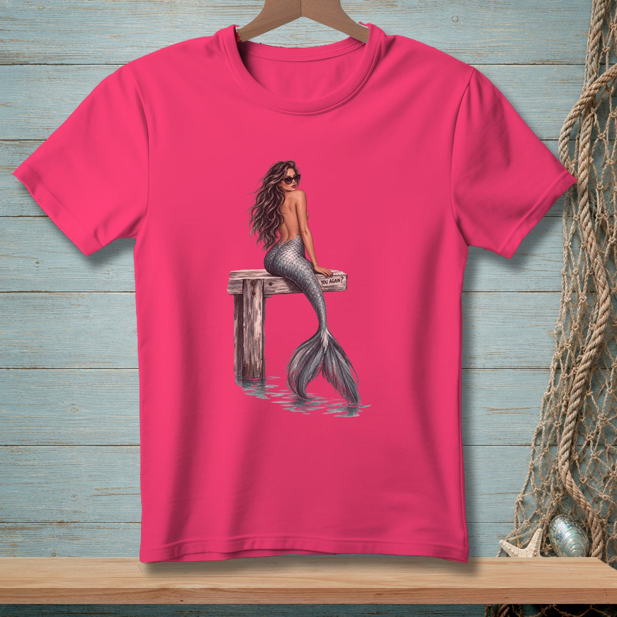 Pink t-shirt with a mermaid sitting on a wooden dock with sunglasses.