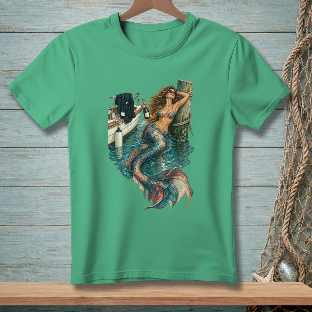 Mermaid with a bottle of champagne leans on a dock post next to a boat.