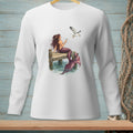 Mermaid on dock holding drink with seagull flying near, on white long-sleeve shirt.