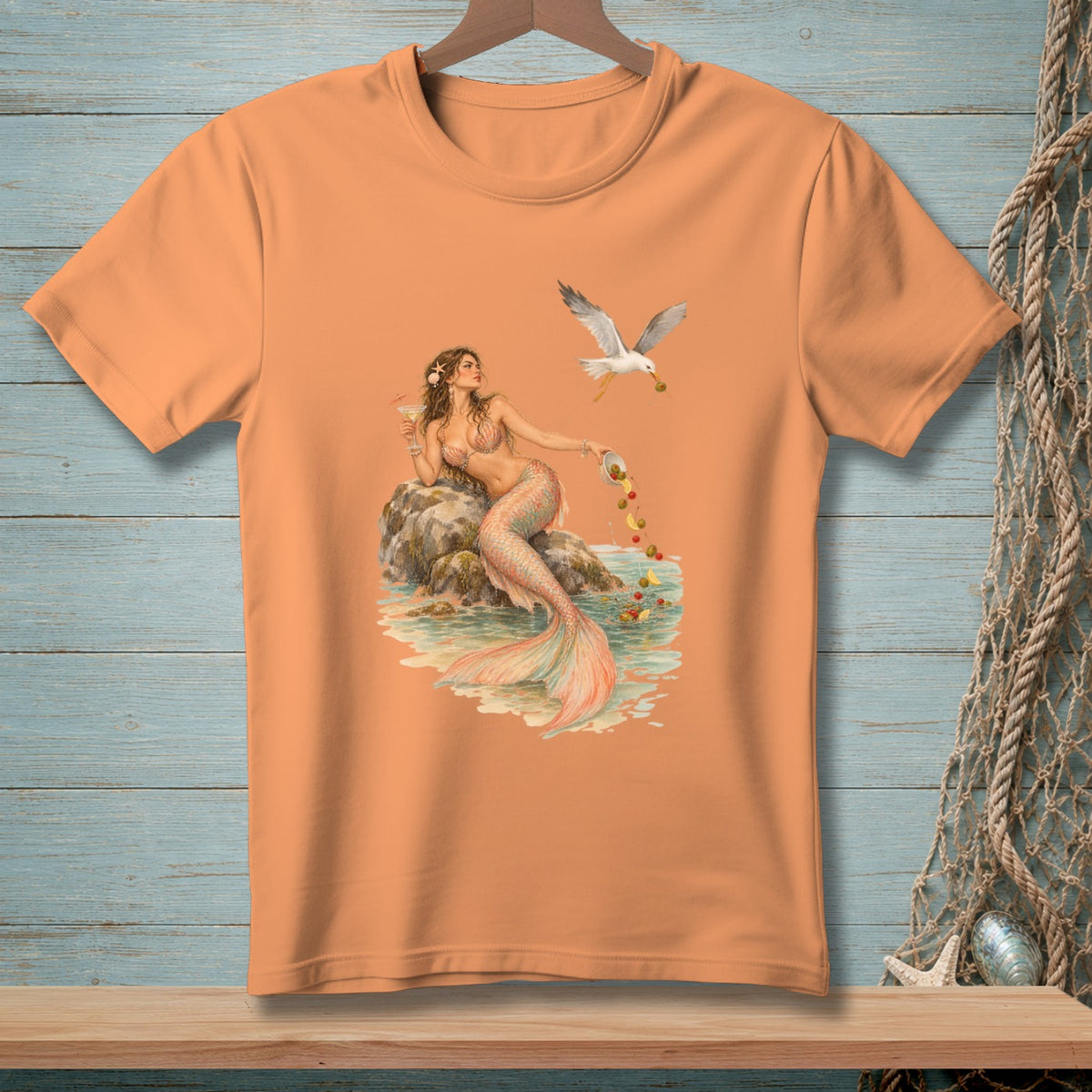 Peach t-shirt with a mermaid holding a drink, by a seagull dropping olives.