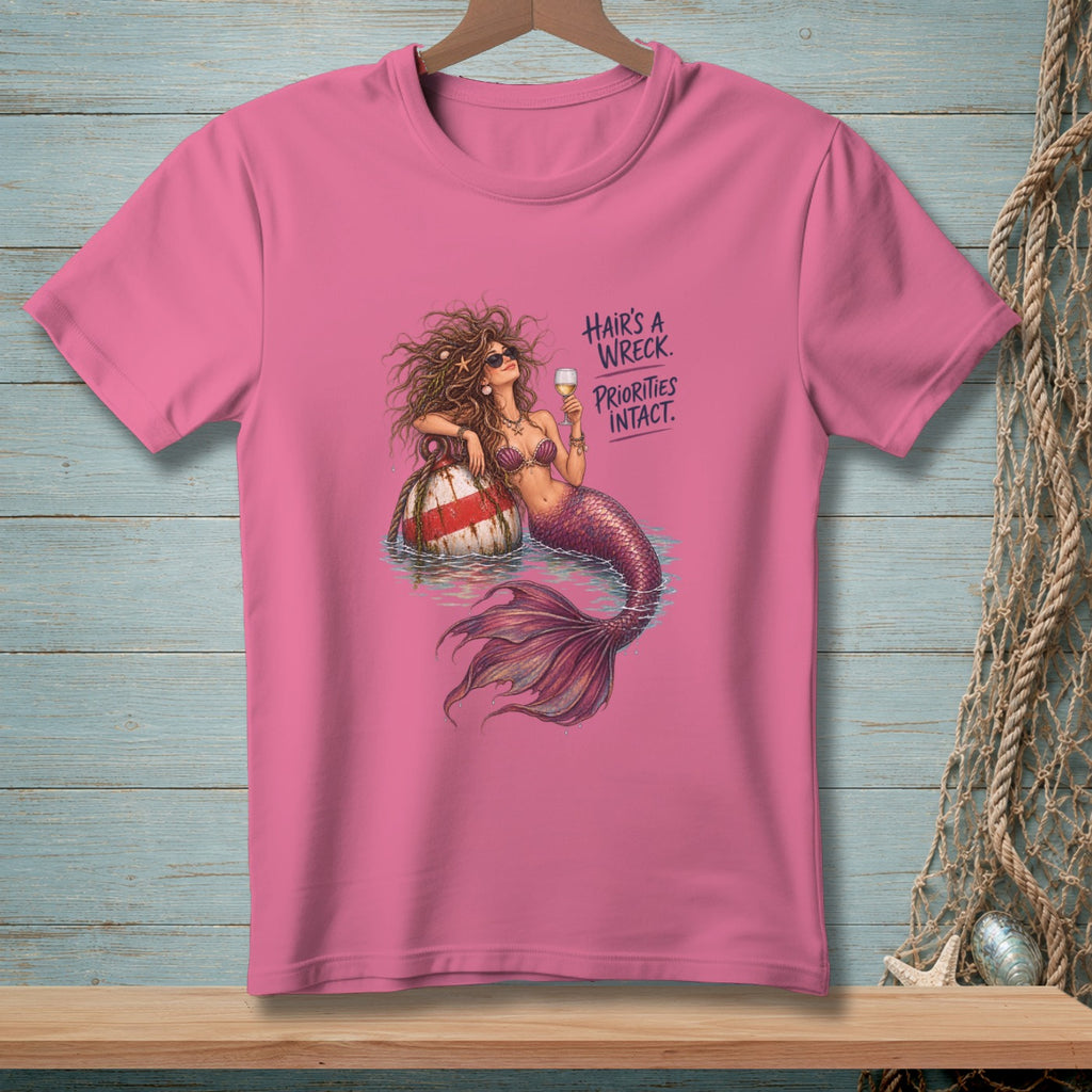 Pink t-shirt with a mermaid sitting on a buoy, holding a drink. Text reads: "Hair's a wreck. Priorities intact."