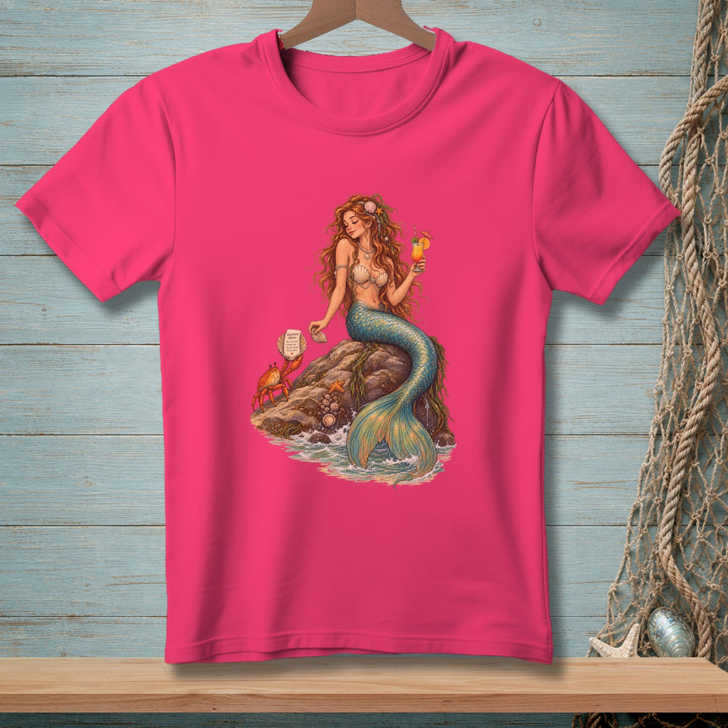 Pink t-shirt with a mermaid holding a drink and a crab on a rock.