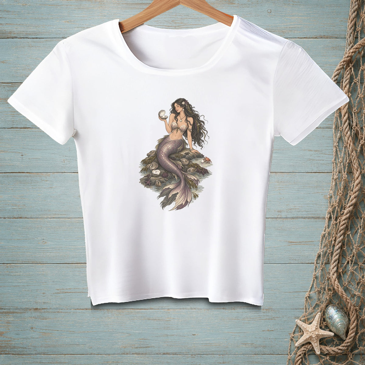 White t-shirt featuring a mermaid holding a seashell, seated on rocks with shells.