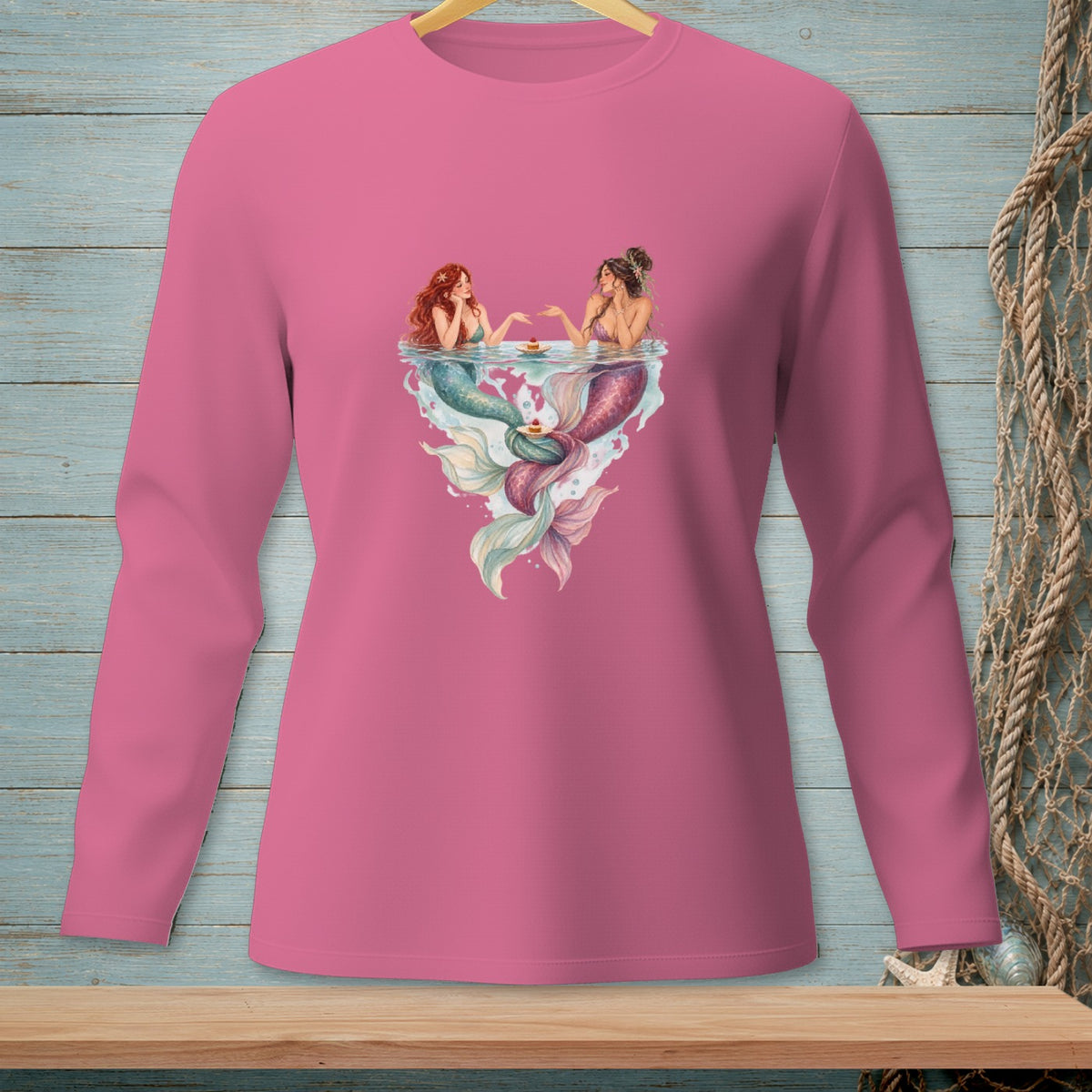 Two mermaids with colorful tails share cupcakes on the water's surface.