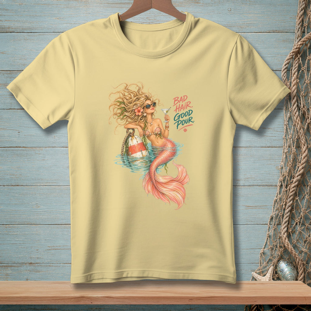 Light yellow t-shirt with a mermaid holding a cocktail and text that reads "BAD HAIR GOOD POUR".