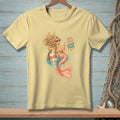 Light yellow t-shirt with a mermaid holding a cocktail and text that reads "BAD HAIR GOOD POUR".
