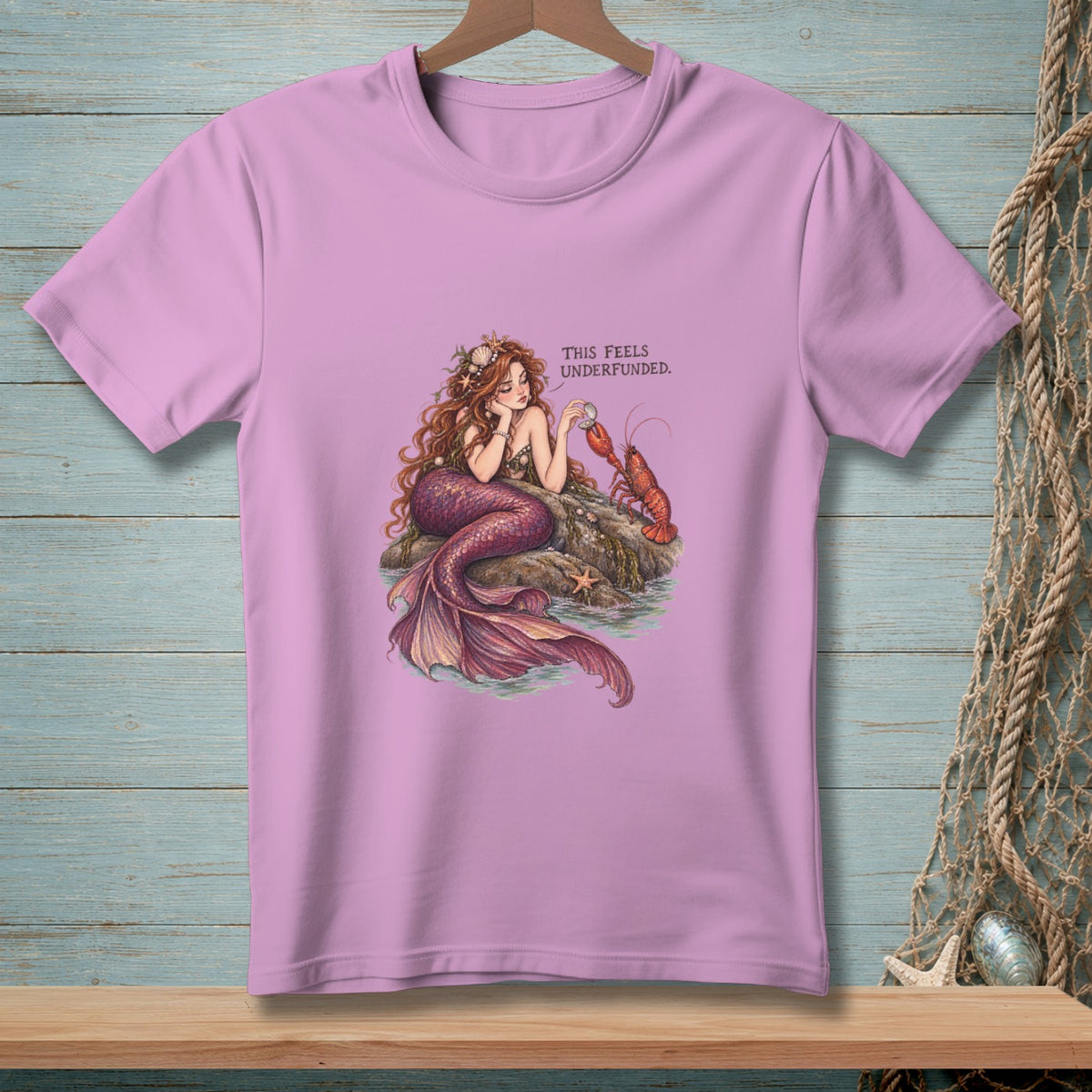 Mermaid with lobster on rock, text reads "THIS FEELS UNDERFUNDED."
