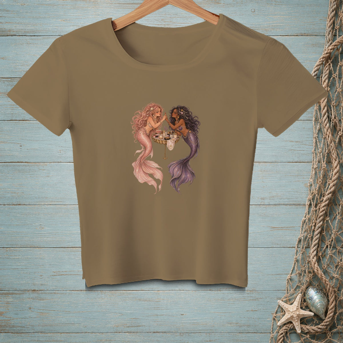 Brown t-shirt featuring a graphic of two mermaids sharing tea on a wooden background.