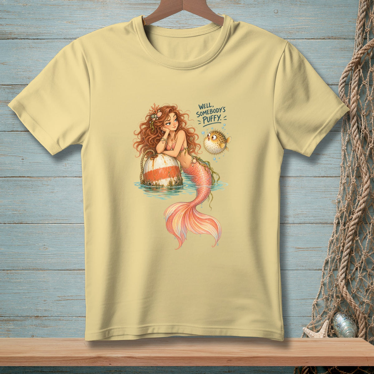Light yellow t-shirt with a mermaid and pufferfish graphic saying "Well, somebody's puffy."