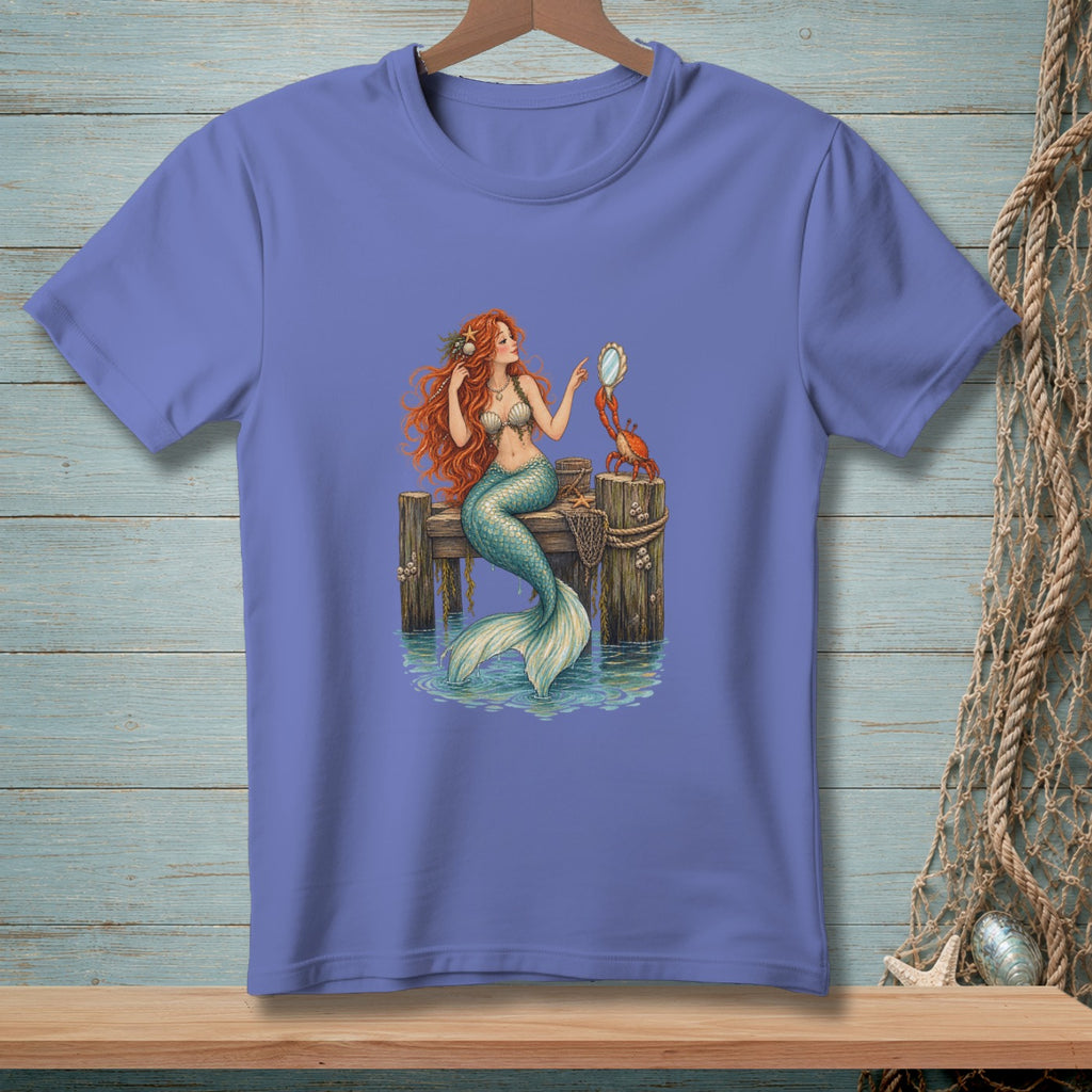 Mermaid with red hair and teal tail sits on dock with a crab holding a mirror.